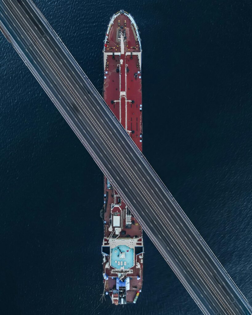 A stunning aerial view capturing a bridge crossing over a large ship in coastal waters.