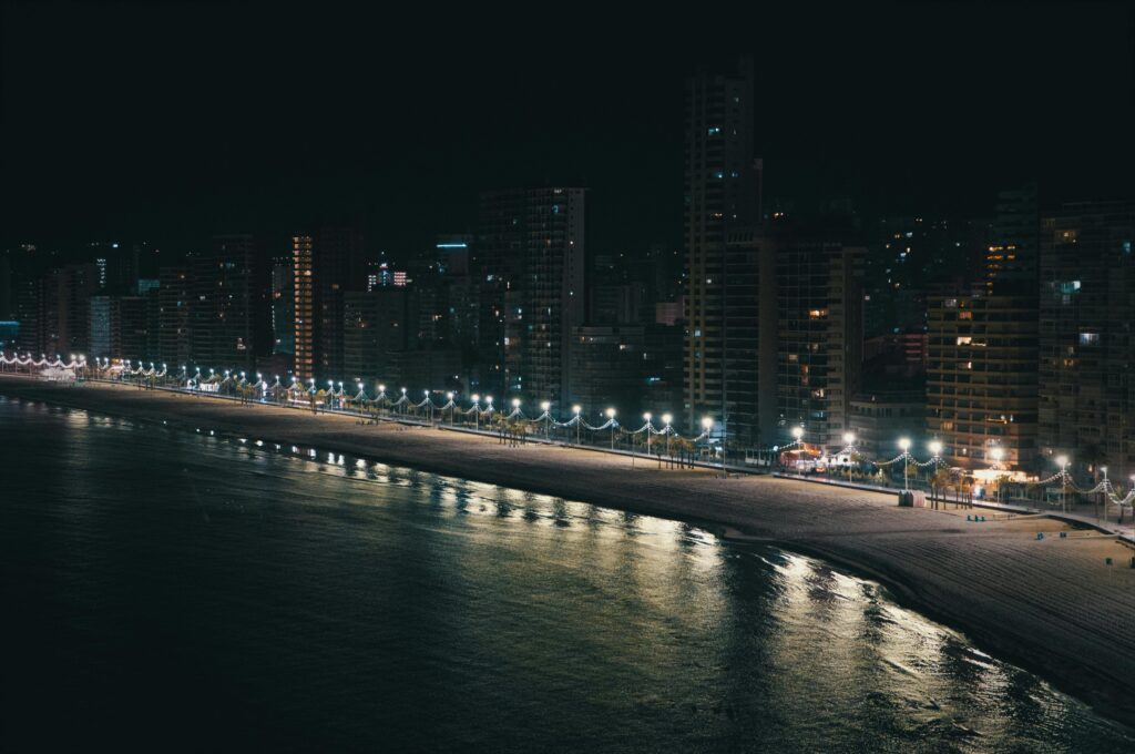 Aerial view of a beachfront city with illuminated buildings and a serene night beach.