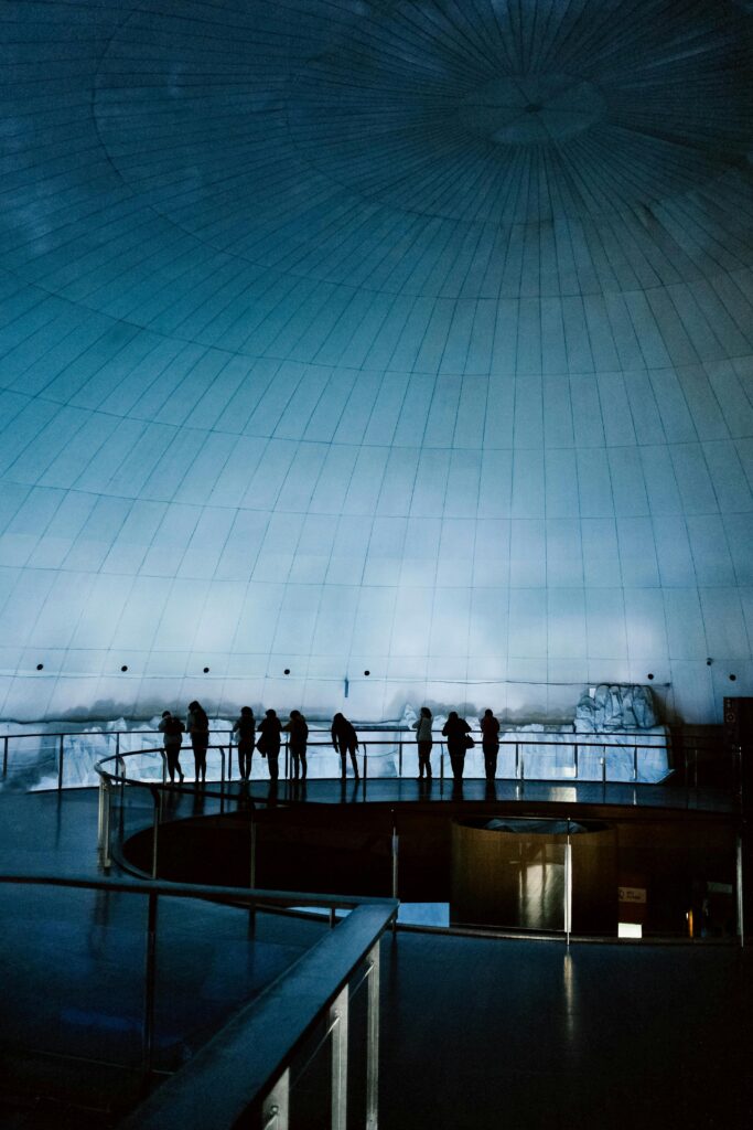 Silhouettes of people observing an underwater dome exhibit, casting an intriguing reflection.